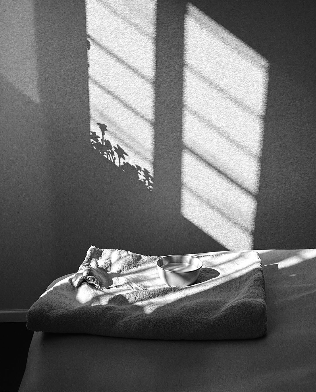 Un linge plié et un bol d'huile sur une table de massage, dans la lumière d'une fenêtre